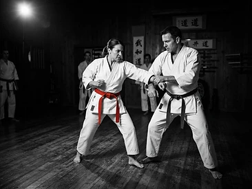 Adult martial arts students practicing a self-defense escape technique in a dark dojo