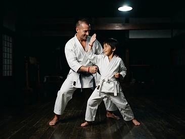Parent and child in martial arts uniforms training together in a dark dojo