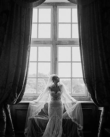Affordable wedding reception photography in Sydney — a bride in a lace gown and veil backlit by a window, captured in editorial black and white