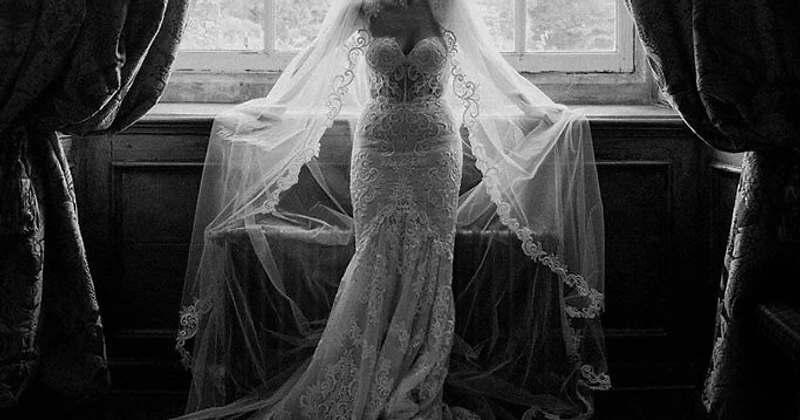 Affordable wedding photography in Sydney — a bride in a lace gown and veil backlit by a window, captured in editorial black and white