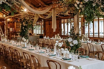 Waldara Farm wedding reception — long banquet tables with white linen and floral centerpieces inside a rustic timber-framed barn with warm string lights at Waldara Farm, Oberon