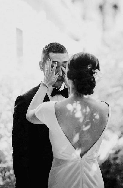 Black and white first look wedding photo — bride playfully covering the grooms eyes before he turns around