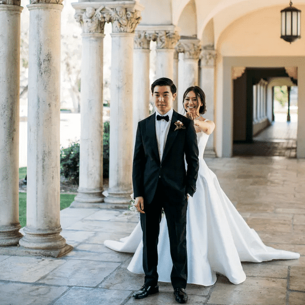 Bride sneaking up behind her groom for a first look in a classic colonnaded walkway