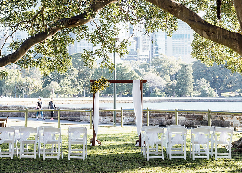Wedding ceremony setup with floral arch overlooking Sydney Harbour and city skyline at the Royal Botanic Garden — Dreams Photography