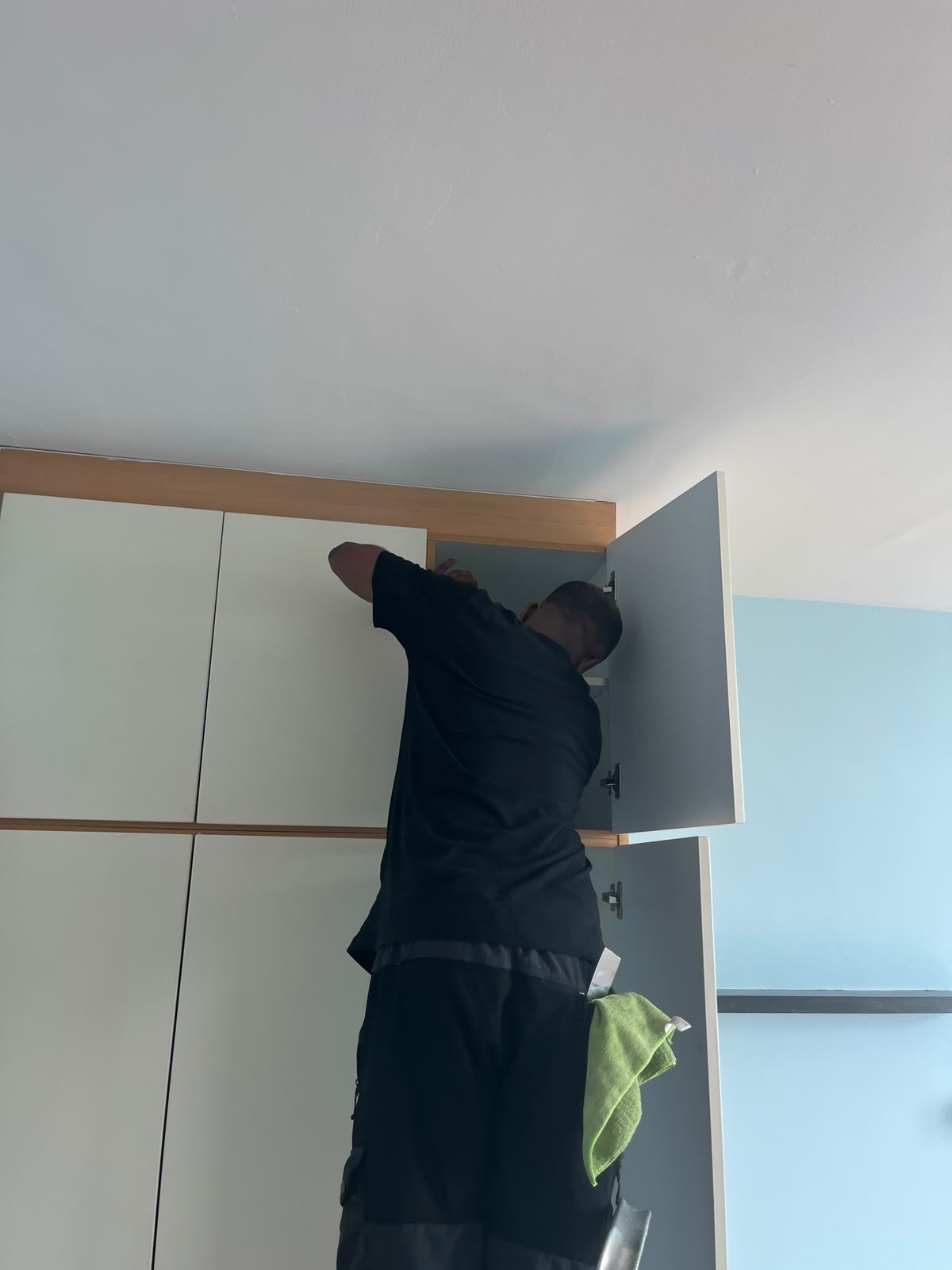 A professional cleaner reaching into an upper kitchen cabinet to clean the interior shelves