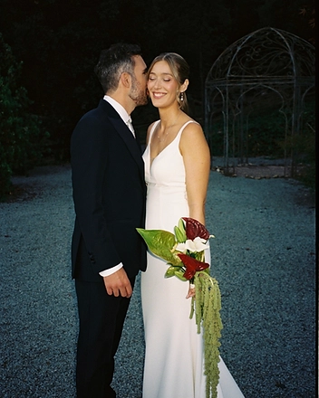 Groom kissing the bride on the cheek by the garden gazebo