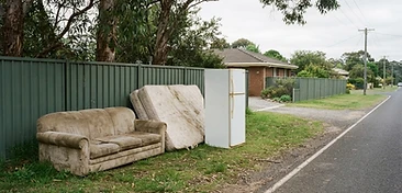 An old couch, a mattress and a retired white fridge placed on a nature strip in a regional Australian street