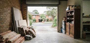 Timber offcuts, plasterboard sheets and packaging stacked on a garage floor during a renovation