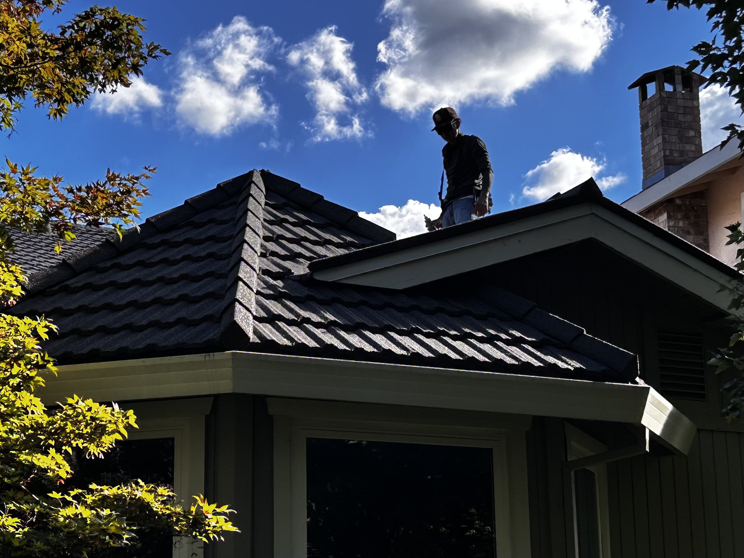 Roofing craftsman working the peak of a tile roof against a clear California sky
