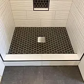 Black hex mosaic shower floor with square drain and white tiled threshold