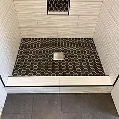 Black hex mosaic shower floor with square drain and white tiled threshold