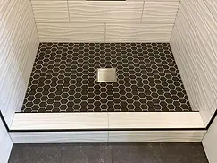 Black hex mosaic shower floor with square drain and white tiled threshold