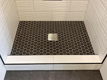 Black hex mosaic shower floor with square drain and white tiled threshold