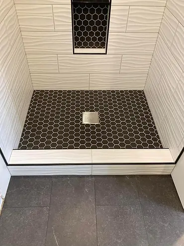 Black hex mosaic shower floor with square drain and white tiled threshold