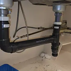 Completed black ABS drain connections beneath a double-basin sink