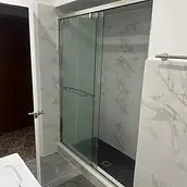 Finished sliding glass shower enclosure with marble-look tile and dark mosaic floor