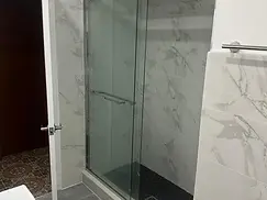 Finished sliding glass shower enclosure with marble-look tile and dark mosaic floor