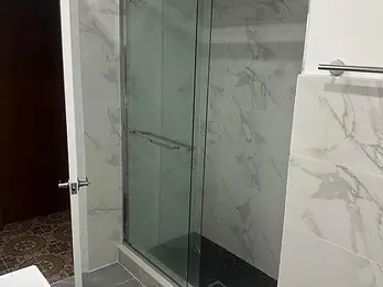 Finished sliding glass shower enclosure with marble-look tile and dark mosaic floor