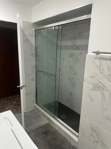 Finished sliding glass shower enclosure with marble-look tile and dark mosaic floor