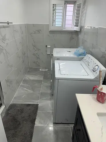 Finished grey bathroom floor tile and wall tile in a combined laundry room