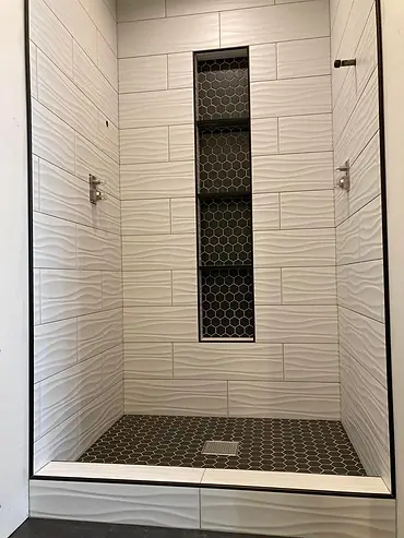 Completed walk-in shower with white textured wall tile, black hex floor tile and recessed niche
