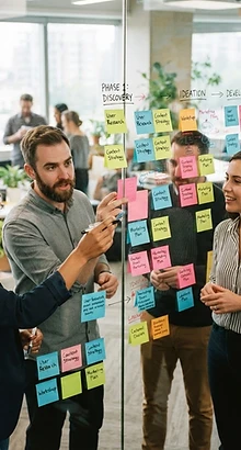 Team collaboratively planning a programme design on a glass whiteboard of sticky notes