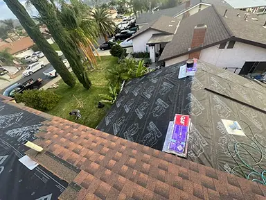 Synthetic roof underlayment with the first brown architectural-shingle courses installed along a hip roof.