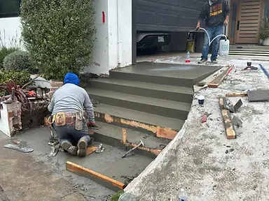 Crew finishing newly placed concrete entry steps at a residential property.