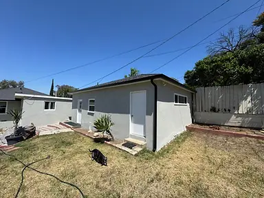 Rear elevation of a light-gray painted stucco home with black gutters and freshly finished white exterior doors.