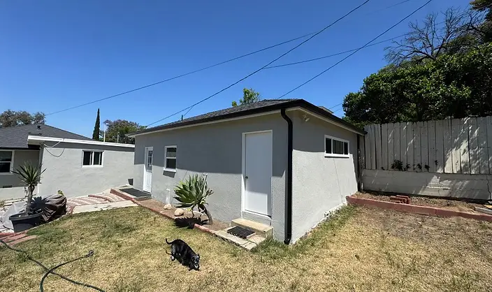 Rear elevation of a light gray painted stucco house with black gutters and freshly painted white doors