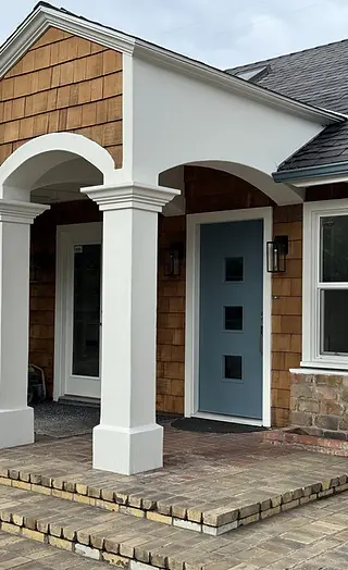 Completed exterior paint job featuring crisp white stucco arches, painted columns, and a slate-blue front door on a cedar shake residence.