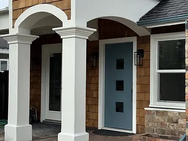 Completed exterior paint job featuring crisp white stucco arches, painted columns, and a slate-blue front door on a cedar shake residence.