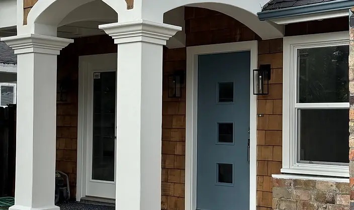 Completed exterior paint job featuring crisp white stucco arches, painted columns, and a slate-blue front door on a cedar shake residence.
