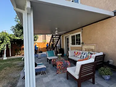 Completed white patio cover with recessed lighting and a ceiling fan above an outdoor seating area.