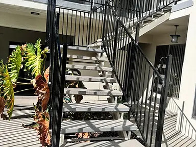 Exterior concrete-tread staircase with black vertical-bar metal guardrail against a stucco wall