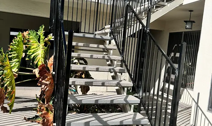 Exterior concrete-tread staircase with black vertical-bar metal guardrail against a stucco wall