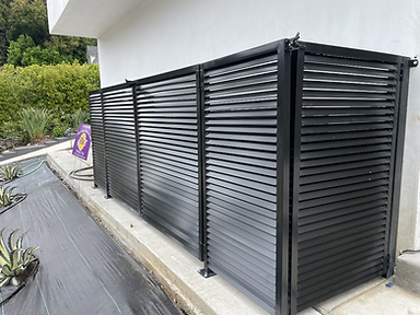 Black louvered metal privacy screen fence panels mounted along a concrete curb