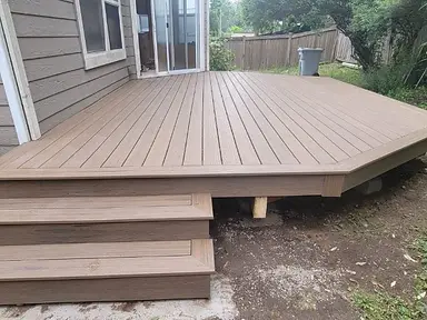 Completed ground-level brown composite deck with a picture-frame edge, angled corner, and three entry steps.