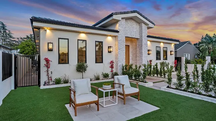 Front yard seating area with turf lawn and landscaping in front of stucco facade at dusk, Valley Glen new construction home.
