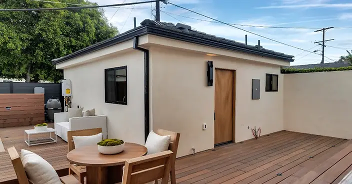 Spacious hardwood deck with teak dining set and lounge furniture beside a new-construction stucco ADU with wood-slat entry door, Valley Glen LA.