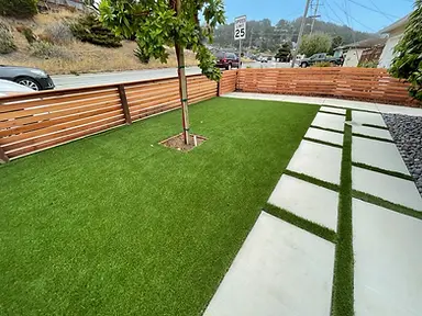 Completed front yard with artificial turf, a shade tree, horizontal cedar fencing, and a concrete-paver walkway with turf joints.
