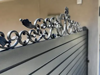 Close up view of decorative wrought iron scrollwork atop a metal gate.