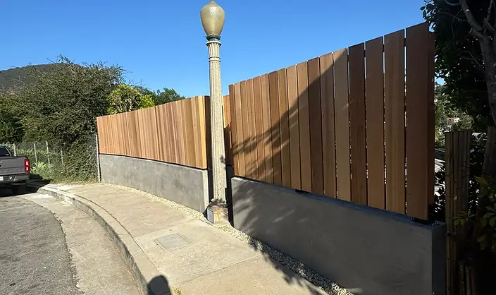 A modern wood slat fence runs along a curved concrete wall.