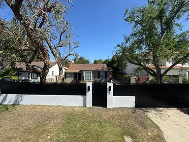 A black metal slat fence with white masonry pillars surrounds a yard.