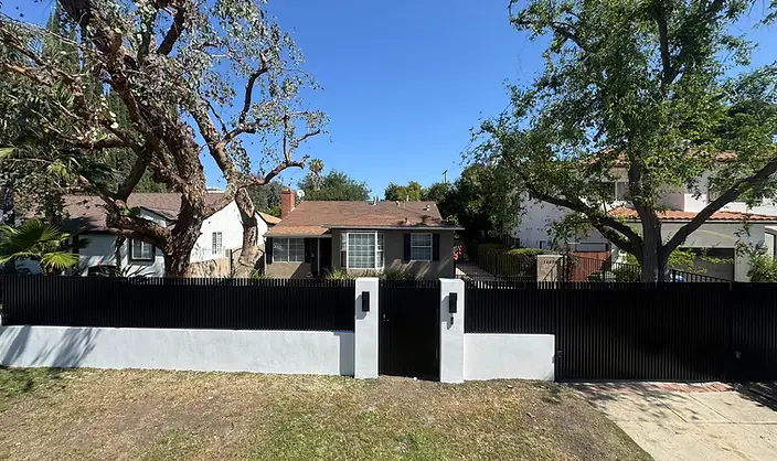 A black metal slat fence with white masonry pillars surrounds a yard.