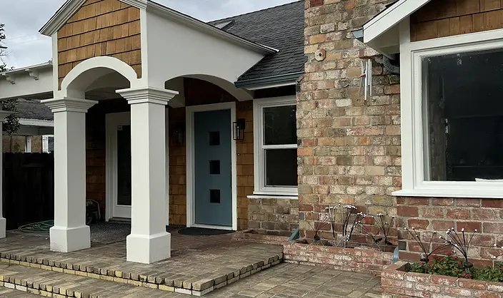Close-up of freshly painted white stucco arched entry portico with decorative columns, slate-blue front door, and brick chimney on a cedar shake exterior.