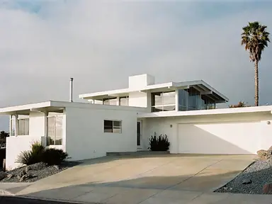 Mid-century modern stucco home with clean white exterior walls, flat rooflines, and a white garage door after painting.