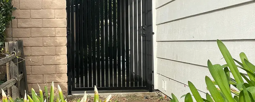 Charcoal pedestrian gate between stone and stucco pillars in Porter Ranch