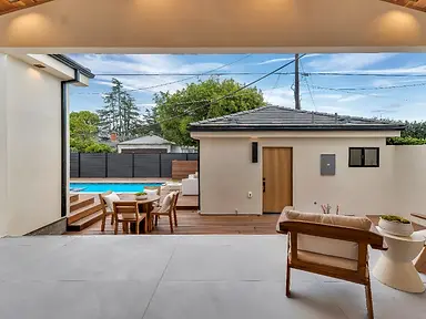 Covered patio with large-format tile and ipe deck leading to pool and stucco cabana in Valley Glen new construction backyard.