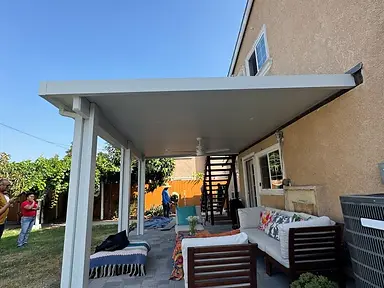 Completed solid white patio cover attached to a stucco home above a gray paver seating area.